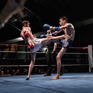 Lead Muay Thai coach at Infinite Martial Arts & Fitness demonstrating the proper Kickboxing technique and power of a teep kick, as he lands a hard strike on his opponent, causing them to crumple under the impact of the kick.