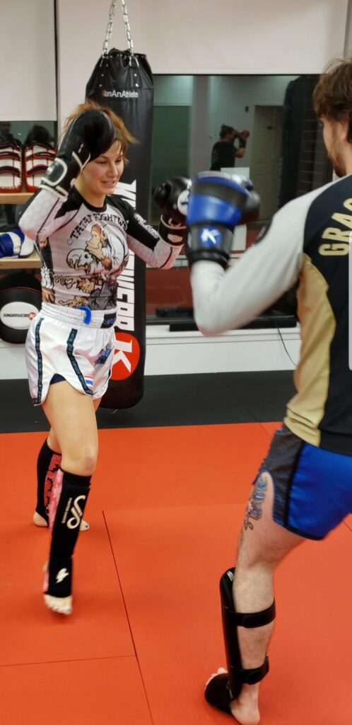 Adorable female Muay Thai fighter training in a small rashguard and traditional Thai shorts at Infinite Martial Arts & Fitness, pushing herself to be the best version of herself.