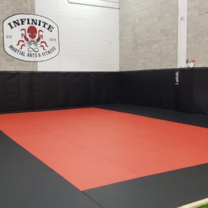 Red and black Brazilian Jiu Jitsu mat space in Belleville's top gym, with black wall mats visible in the background.