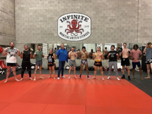 The elite fight team of Infinite Martial Arts & Fitness Gym, covered in sweat and determination after a grueling sparring session. The team's dedication and hard work is evident in their impressive physiques and fierce expressions