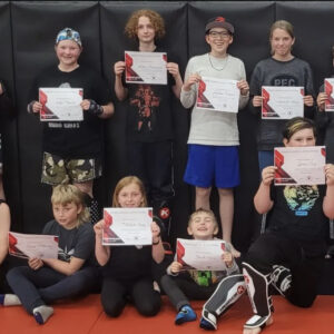 Excited kids line up, holding their newly earned Muay Thai certificates in a grading ceremony at Infinite Martial Arts & Fitness
