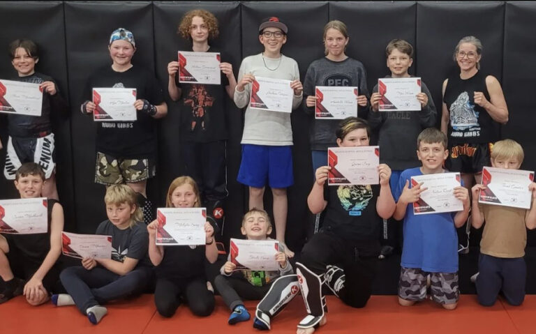 Excited kids line up, holding their newly earned Muay Thai certificates in a grading ceremony at Infinite Martial Arts & Fitness