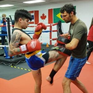 A Muay Thai fighter from Infinite Martial Arts and Fitness demonstrates precision and power as they throw a knee strike on their coach during a training session.
