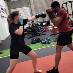 Female boxer receiving expert training from a coach, learning and perfecting the fundamentals of boxing including footwork, stance, and punch technique at a Belleville boxing gym.