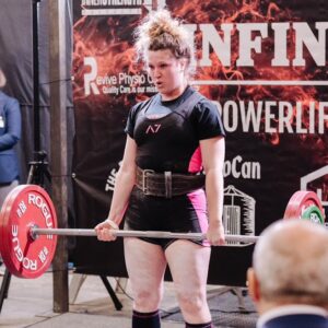 A fit woman deadlifting a significant weight in a singlet at a powerlifting competition. She is focused and determined as she lifts the barbell.