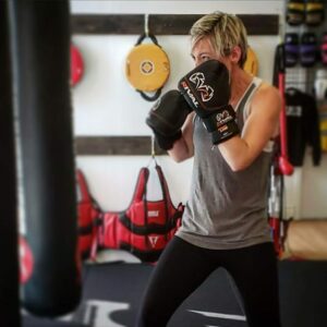 Female boxer training hard at a Belleville boxing club, hitting a heavy bag with focus and determination, working on strength and technique."