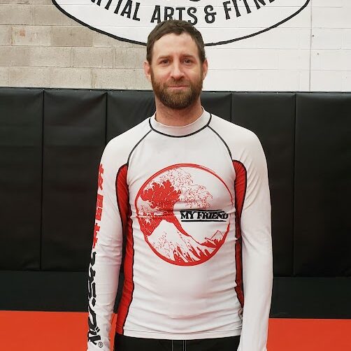 BJJ instructor at Infinite Martial Arts & Fitness in a white nogi rashguard demonstrating technique.