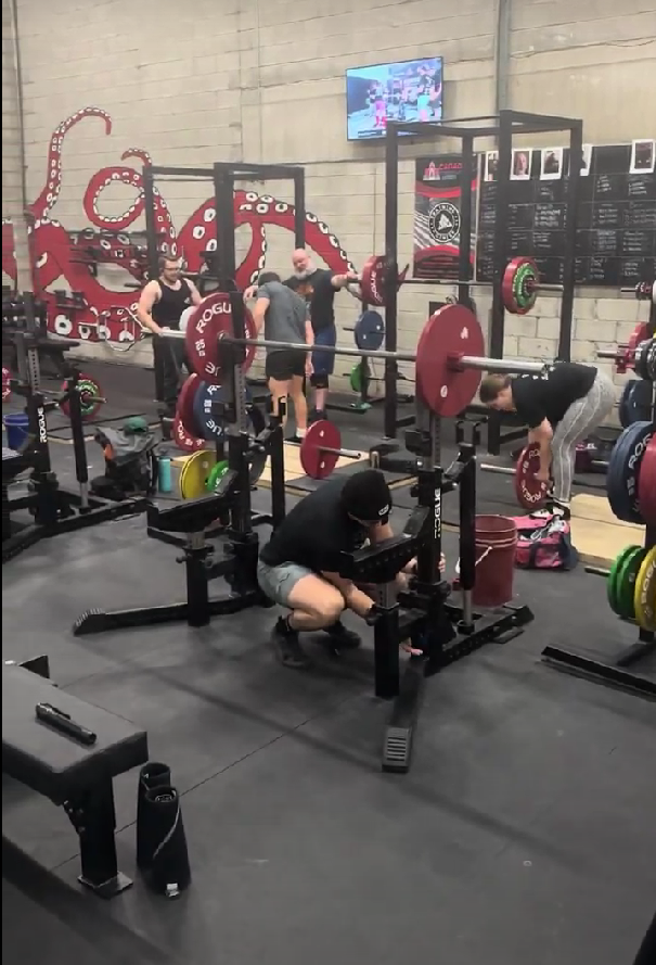 Inside the gym, multiple powerlifters are actively training in the open gym area, using various strength equipment, showcasing the gym's dynamic and focused training environment.